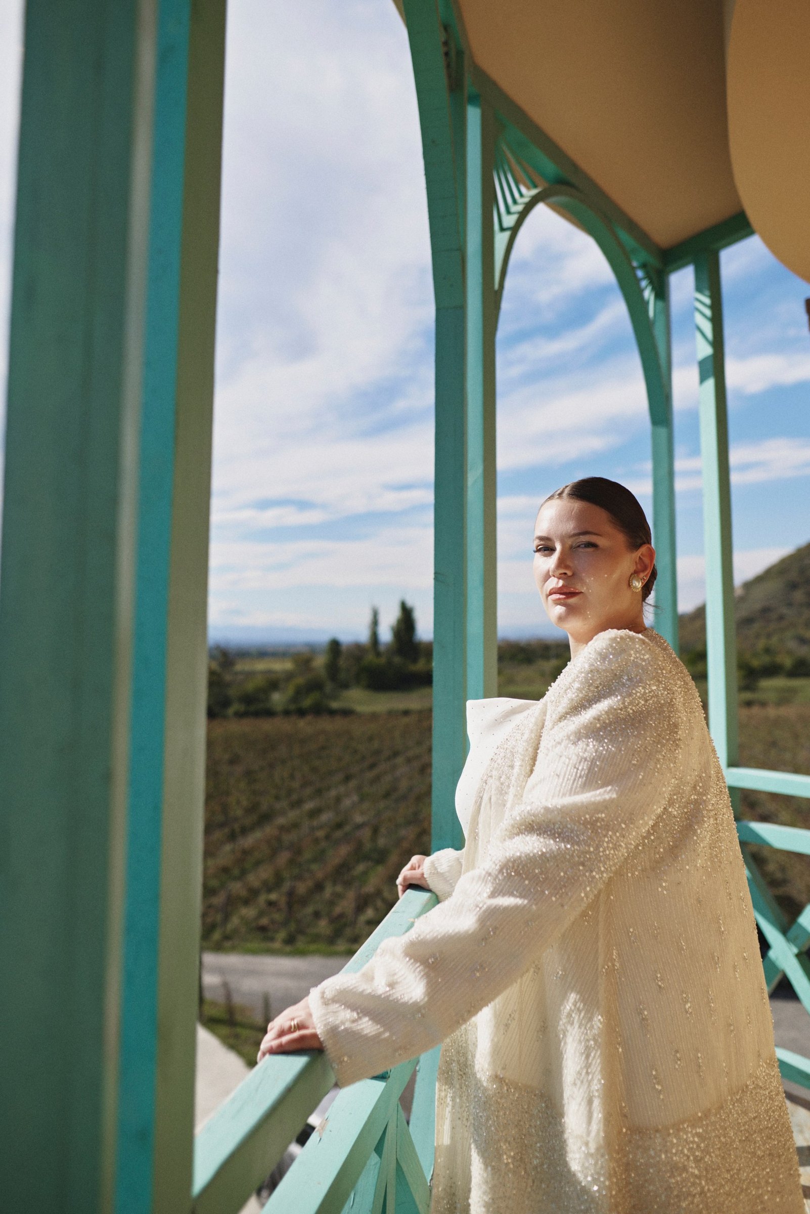 Bride in a sparkling coat on the turquoise balcony above the vineyards