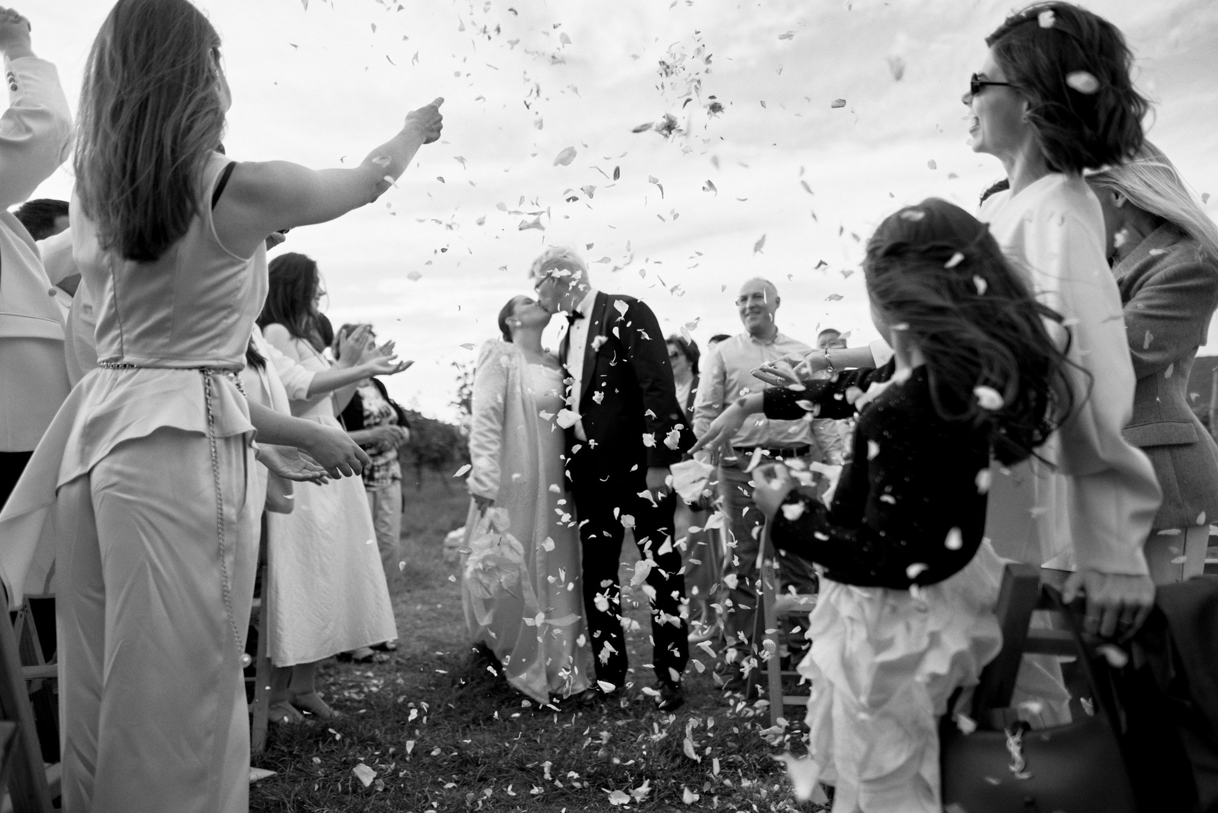 Guests toss confetti over the newlyweds between the vineyard rows