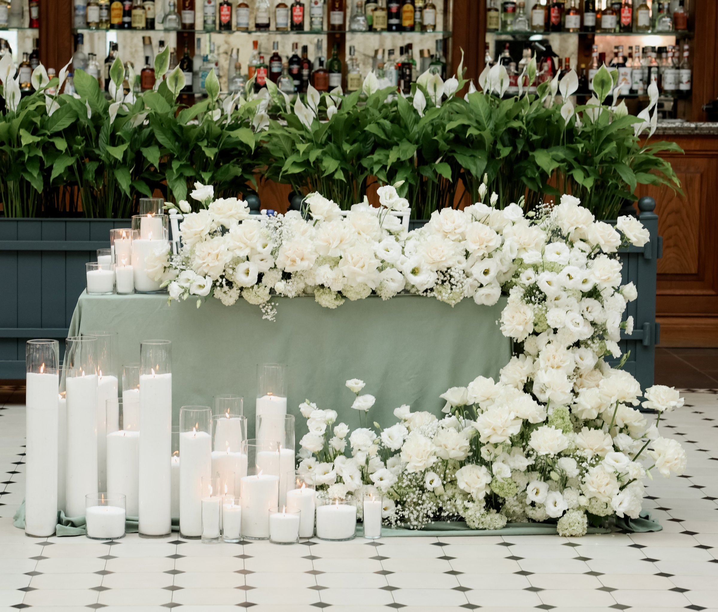 White floral bank with pillar candles at the ceremony entrance