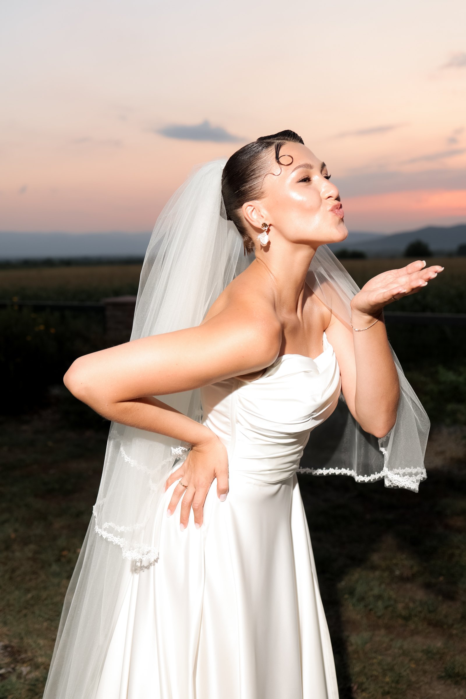 The bride blows a kiss into the sunset