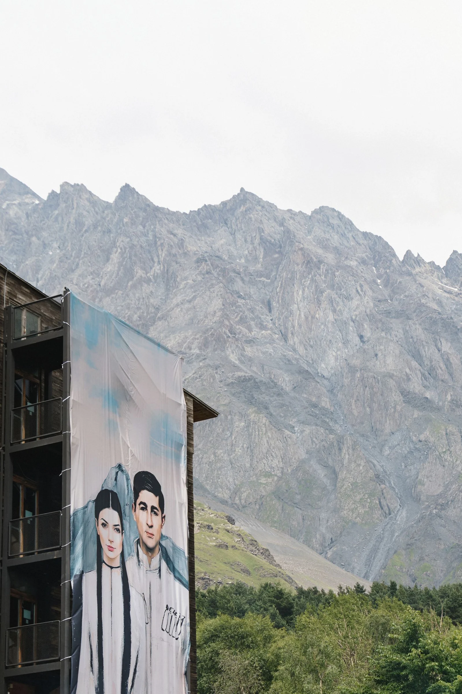 A hand-painted banner of the couple on the hotel facade under the Kazbegi ridge