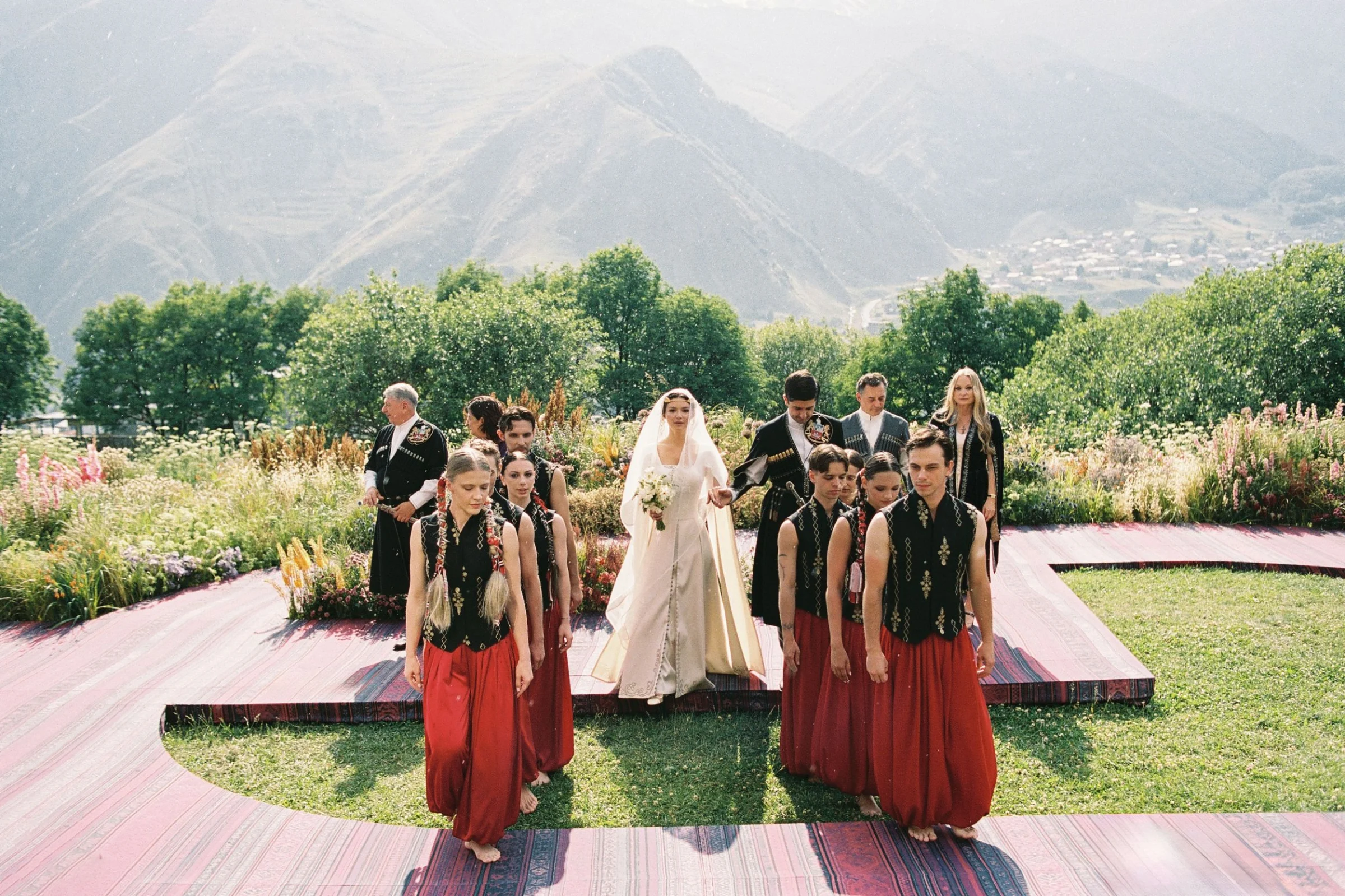 The bride walks in behind Georgian dancers, the ridge behind them